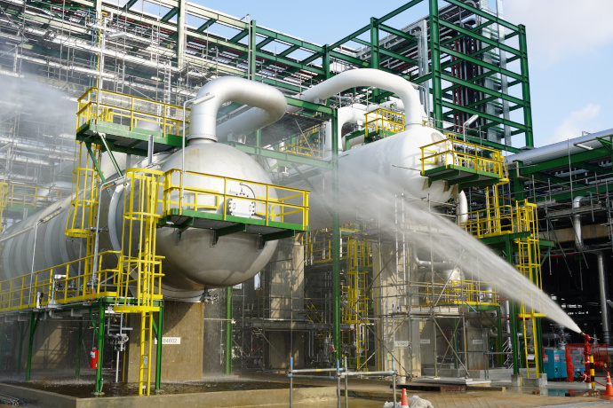 Industrial cleaning and maintenance: Complex industrial facility with large tanks, pipes, and scaffolding, with a jet of water being sprayed from a tank.