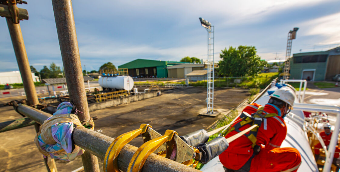 A male worker is wearing a safety harness clipped to a handrail
