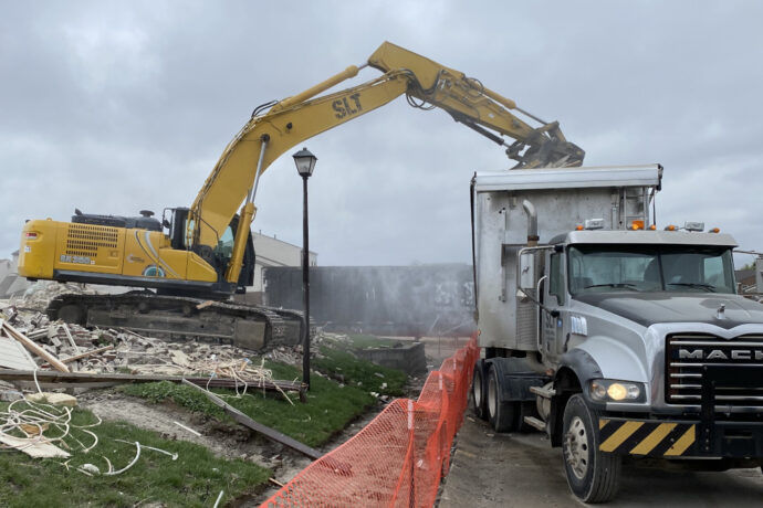 Exterior demolition in progress: excavator loading rubble into a truck.