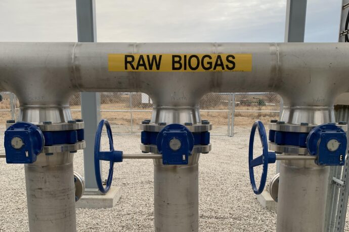 Biogas infrastructure, including pipes with valves surrounded by chainlink fence.