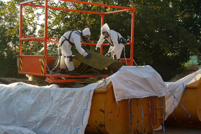 Workers in safety gear handling potentially hazardous material in compliance with asbestos removal regulations.