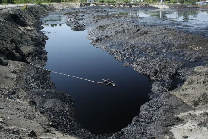 Environmental remediation: Open pit filled with dark, potentially oil-like substance, cable stretching across, indicating a contaminated site needing remediation.